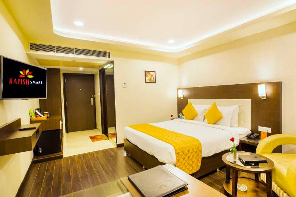 A hotel room with a bed, a desk, a chair, a TV, and a door.