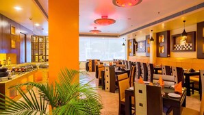 A restaurant with multiple dining tables and chairs, a bar area with various items, and a large window providing natural light. - Hotel Kapish Smart (Jaipur)
