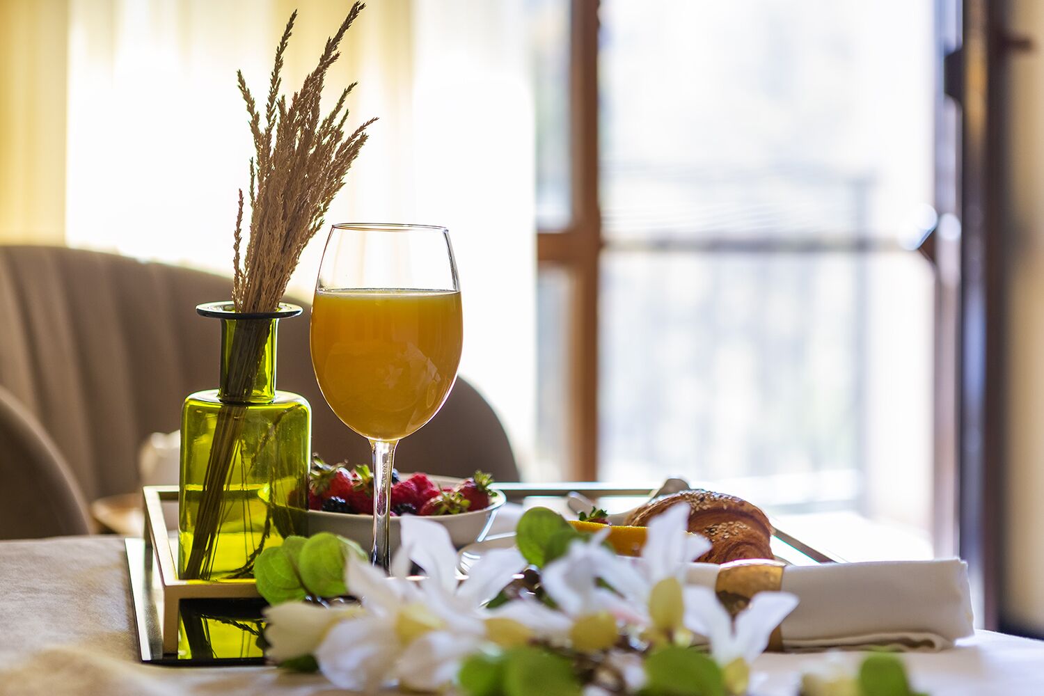 A table with a glass of orange juice, a bowl of berries, a croissant, and a vase with dried plants.