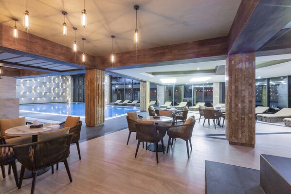 Un espace piscine intérieur moderne, doté de coins salon et d’un bar.