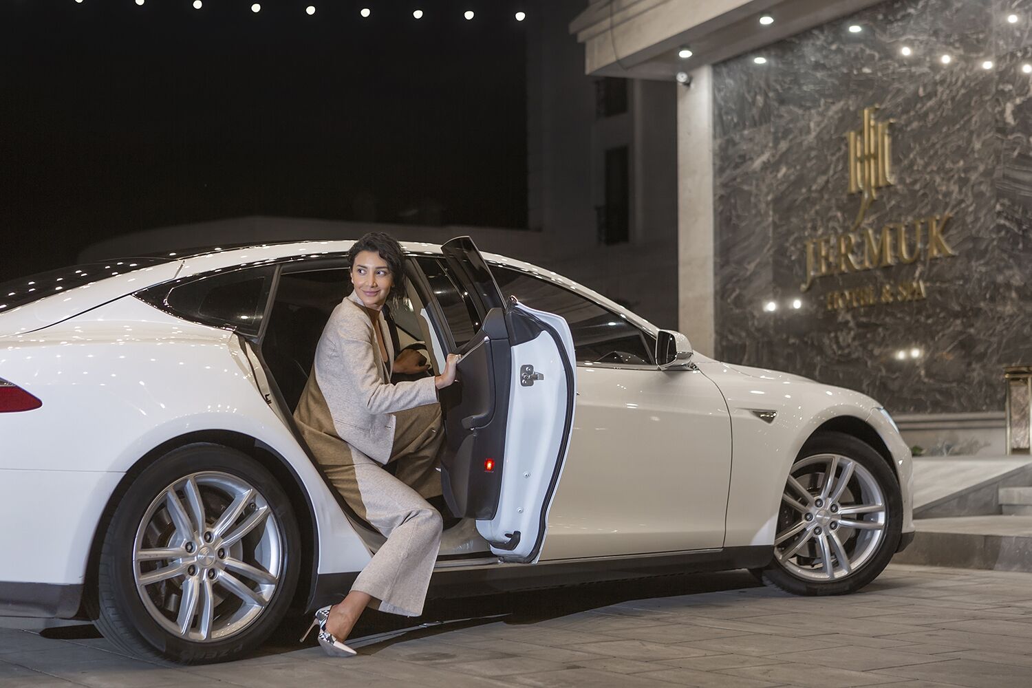 A white luxury car parked in front of a building with a marble facade and the name "FREMUK" visible.