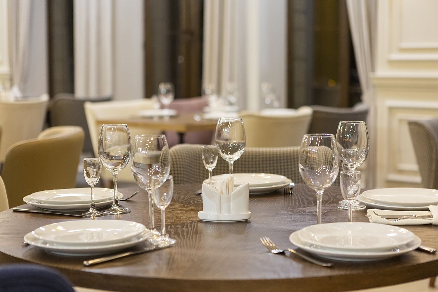 A dining table set with white plates, clear wine glasses, and cutlery.