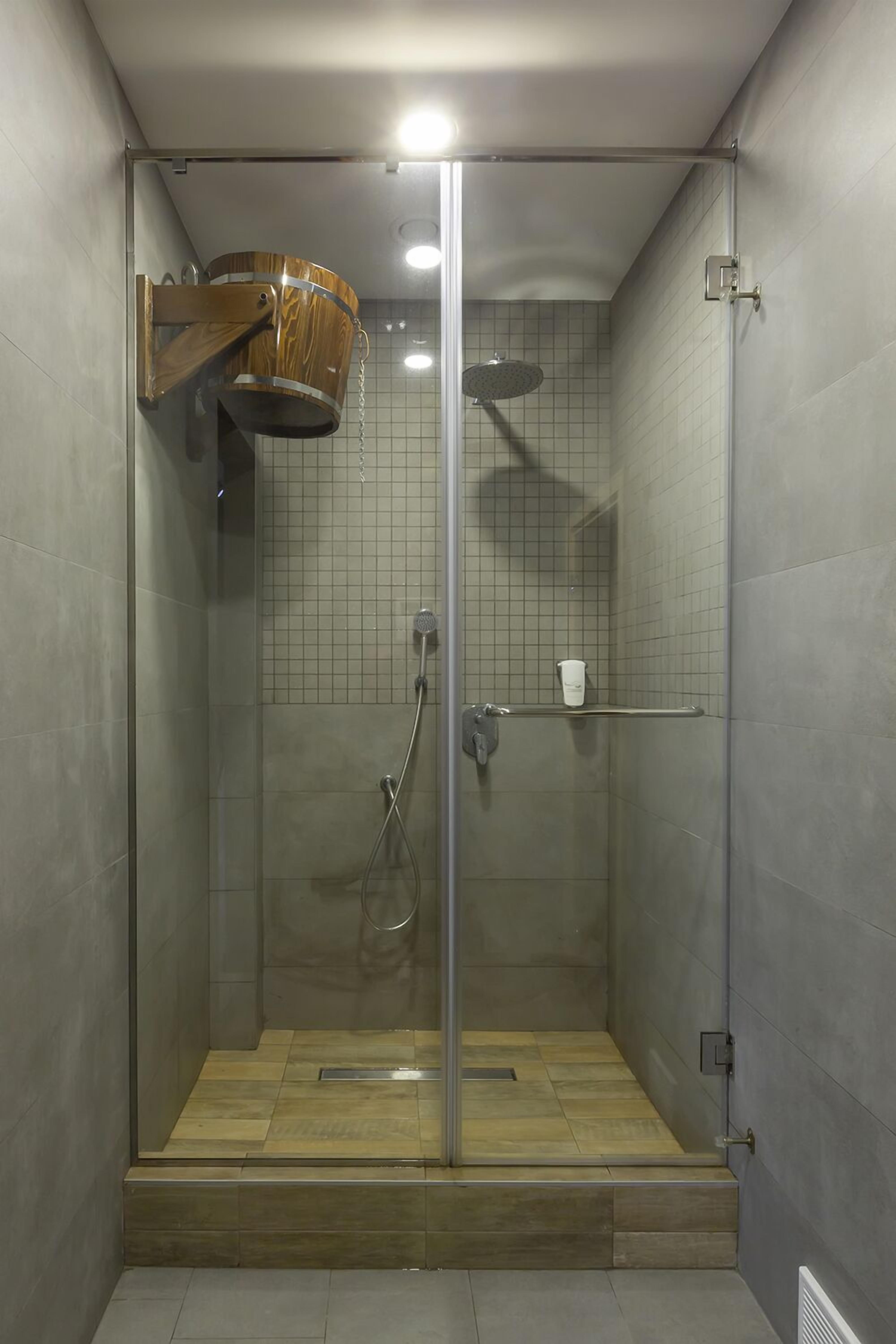 A glass-enclosed shower with a wooden bucket, a handheld showerhead, and a towel rack.