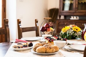 A dining table with plates of pastries, a bowl of fruit, and a vase of sunflowers.