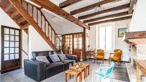 A spacious living room with a black leather sofa, wooden coffee tables, and blue chairs. A wooden staircase leads to an upper level.