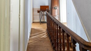 A wooden staircase with a railing leading to a room with a large wooden clock and a desk.