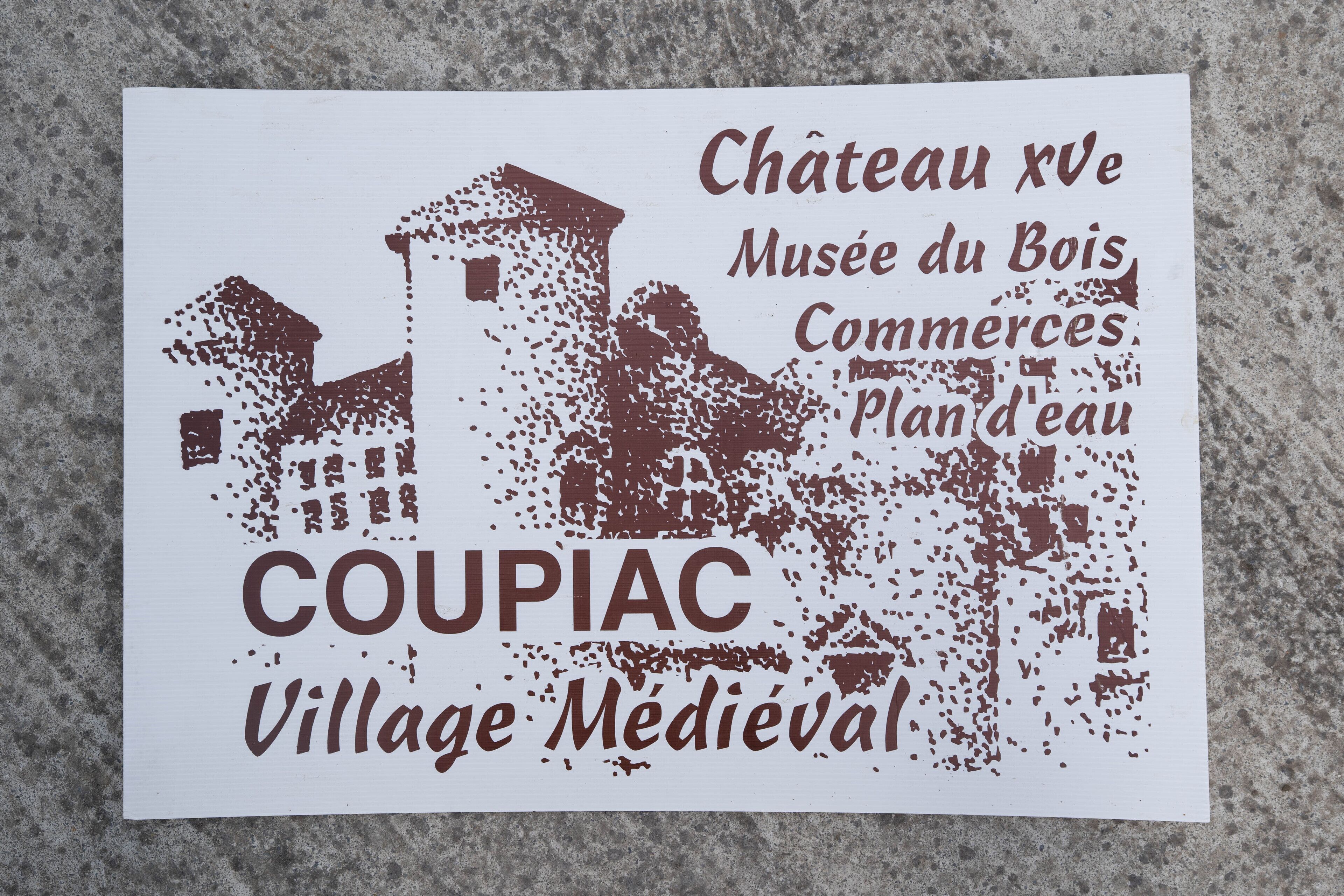 Een bord met tekst in het Frans, met vermelding van Chateau XVe, Musee du Bois, Commerce, Plan d'eau en Coupiac Village Medieval.