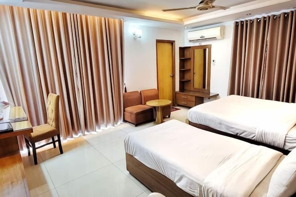 A hotel room with two beds, a desk, a chair, a sofa, a small round table, and a wardrobe.
