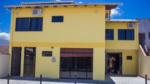 A two-story yellow building with a tiled roof, a gated entrance, and a visible number '38' on the wall. - Pousada Sol de Maria (Penha)