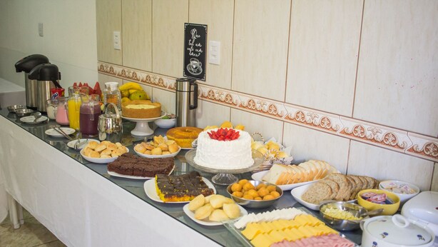 A buffet table with various food items including cakes, breads, and cheeses. - Pousada Sol de Maria (Penha)