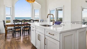Una cucina con una grande isola, mobili bianchi e vista sull'oceano.