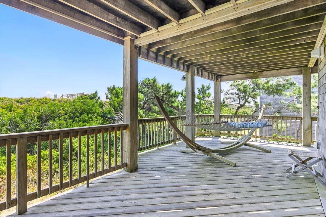 A wooden deck with a hammock, railing, and a view of greenery.