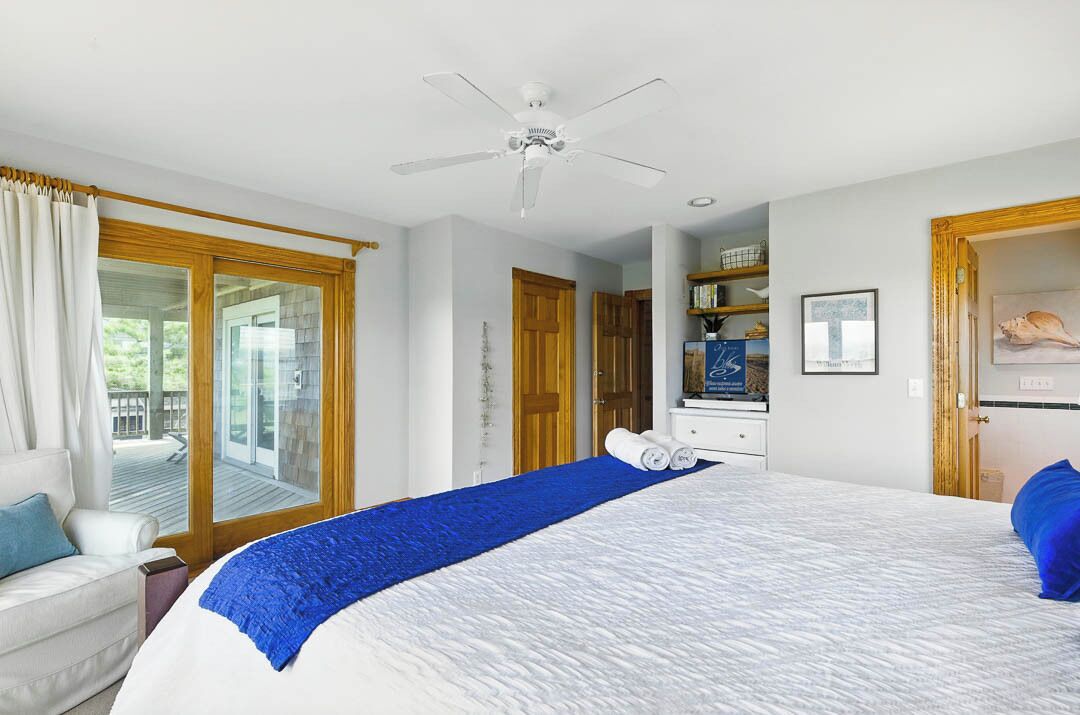 A hotel room with a large bed, a ceiling fan, a sliding glass door to a balcony, and a wooden door.