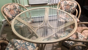 A round glass table surrounded by four floral-patterned chairs with metal frames. - Fisherman's Cabin on the Bay (Norfolk)
