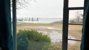 A view from a room with a large window overlooking a body of water, a dock, and some vegetation. - Fisherman's Cabin on the Bay (Norfolk)