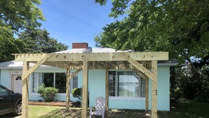 A wooden pergola structure in front of a light blue house with a brick chimney. - Fisherman's Cabin on the Bay (Norfolk)