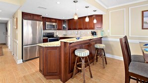 A kitchen with wooden cabinets, stainless steel appliances, a granite countertop, and a bar stool.