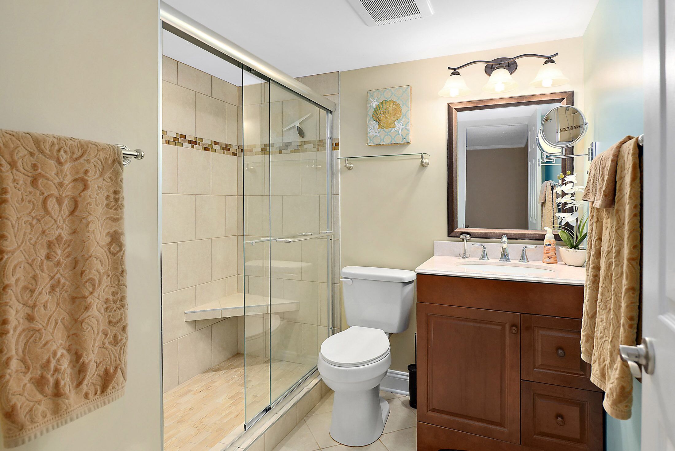 A bathroom with a glass shower enclosure, a toilet, a vanity with a mirror, and a towel rack.