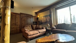 Ein gemütliches Wohnzimmer mit einem braunen Ledersofa, einem Holztisch und einem großen Fenster mit Blick auf Bäume.