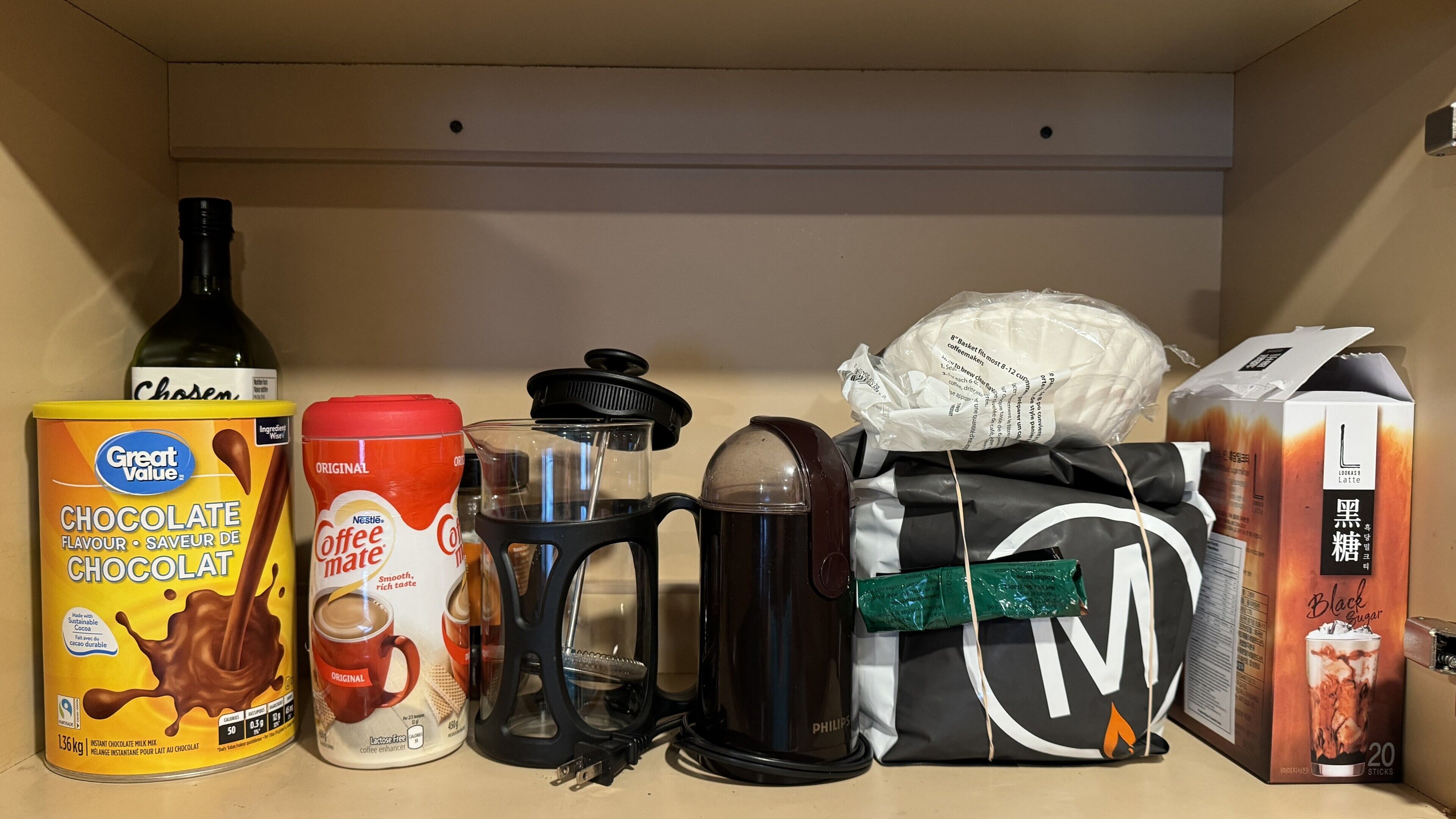 Une étagère de cuisine contenant divers articles liés au café, notamment une tasse à café de la marque Nestlé, une machine à café, une boîte de sucre noir et un carton de lait.