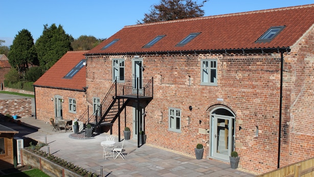 Een bakstenen gebouw met een pannendak, een trap die naar een balkon leidt en een terras met tuinmeubilair.