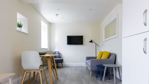 Een moderne woonkamer met een grijze bank, een bijzettafeltje, een blauwe stoel en een aan de muur bevestigde televisie.