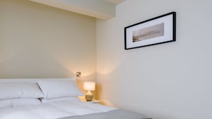 Een netjes opgemaakt bed met witte lakens en een grijze plaid, een bedlampje en een lijst met een foto aan de muur.