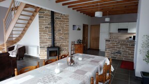 A cozy living room with a stone wall, a fireplace, wooden furniture, and a staircase. - Charming cottage near the sea (Saint-Germain-sur-Ay)
