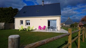 A two-story house with a sloped roof, a balcony with outdoor seating, and a fenced yard. - Charming cottage near the sea (Saint-Germain-sur-Ay)