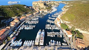 An aerial view of a coastal town with a marina filled with boats, a castle, and surrounding greenery. - Air-conditioned 75m2 duplex with spa and panoramic views! (Porto-Vecchio)