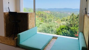 A room with a large window offering a view of a forested landscape and mountains. - Air-conditioned 75m2 duplex with spa and panoramic views! (Porto-Vecchio)