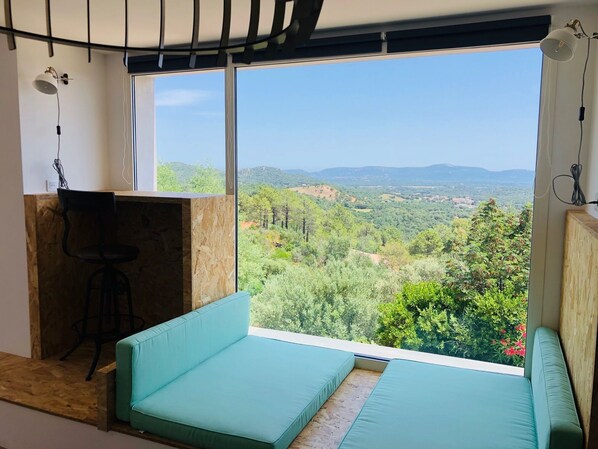 A room with a large window offering a view of a forested landscape and mountains.