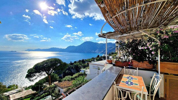 Une terrasse avec vue sur la mer, une table avec des chaises et des plantes en pot.