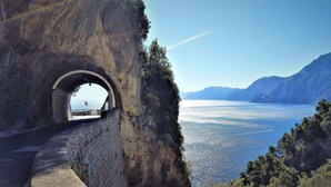Un arc en pierre mène à un point de vue offrant une vue sur une mer calme et des montagnes lointaines.