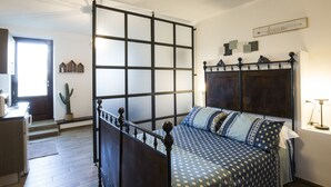 A bedroom with a bed, a nightstand, a lamp, a window, and a door.