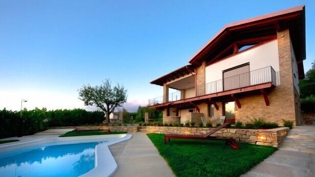 A modern two-story house with a swimming pool, stone exterior, and a well-maintained lawn.