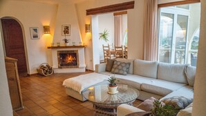 Una sala de estar acogedora con chimenea, un sofá, una mesa de centro redonda de vidrio y vistas al exterior.
