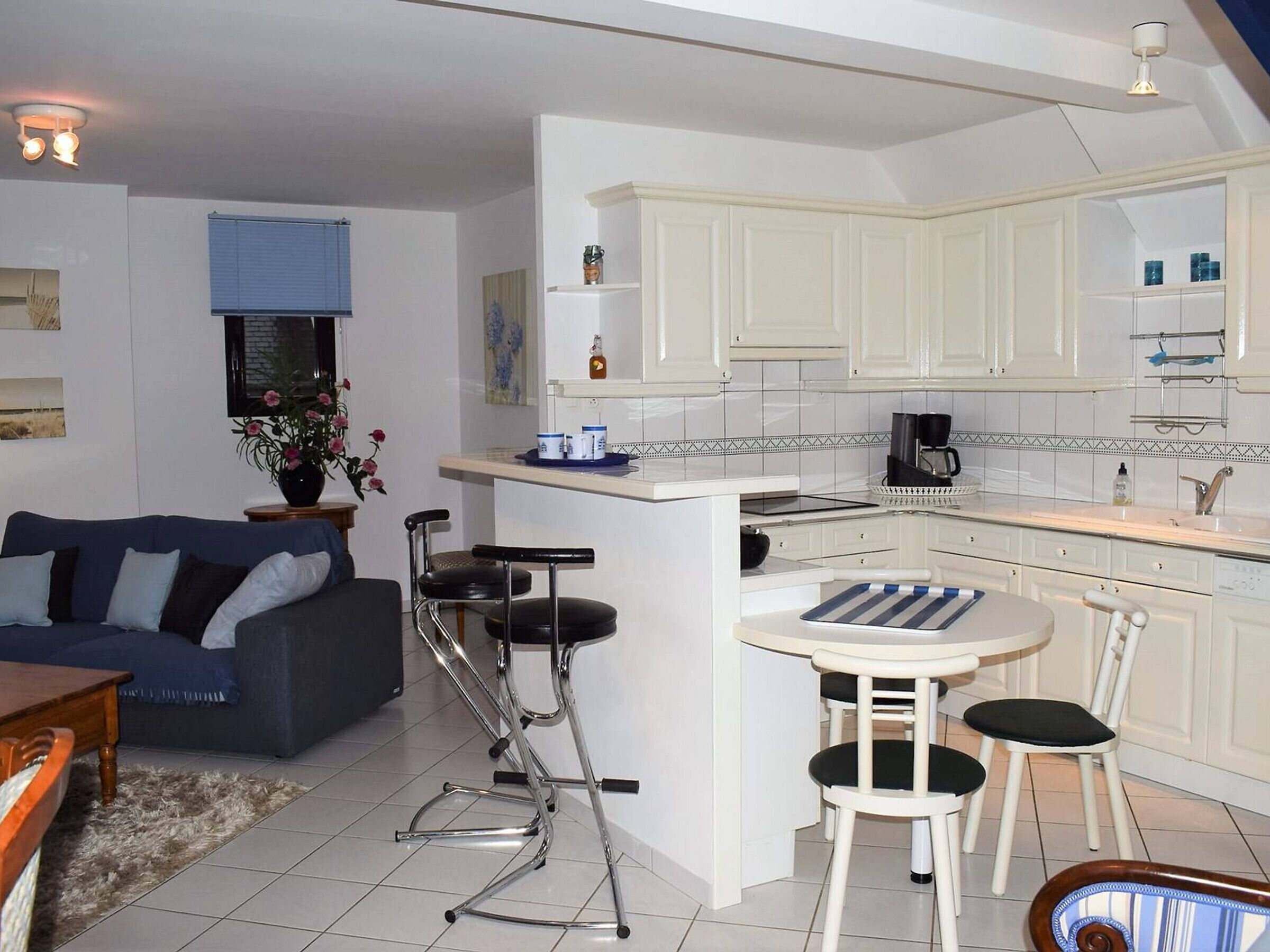 Un espacio habitable compacto con kitchenette, una zona de comedor con una mesita y sillas, y un sofá en la sala.
