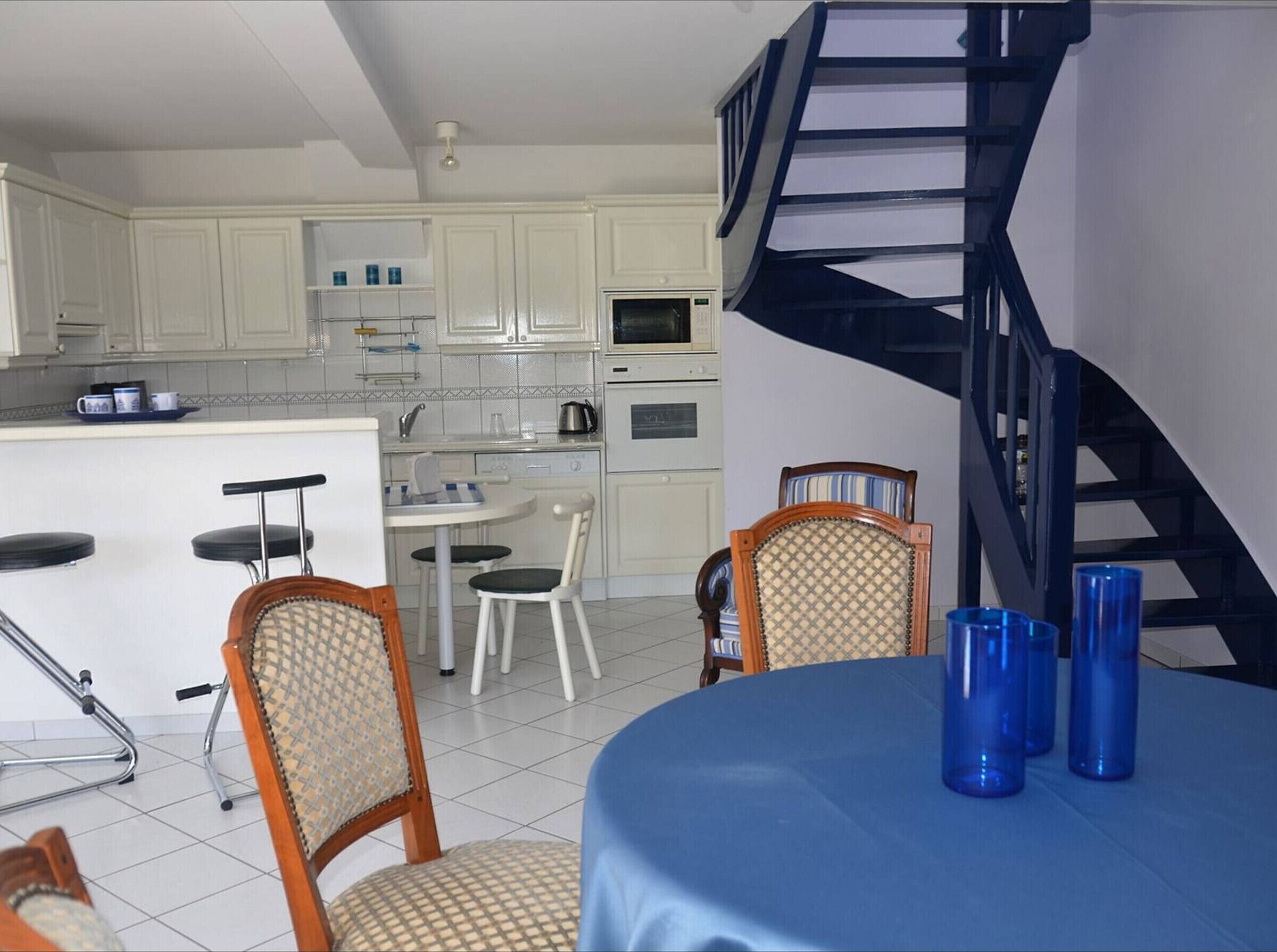 A modern kitchen with white cabinets, a dining area with a blue tablecloth, and a spiral staircase.