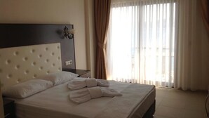 A hotel room with a large bed, a headboard, a nightstand, and a view of the city through sheer curtains. - Yılmaz Kaptan Otel (Marmaris)