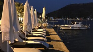 A row of sun loungers with white umbrellas on a wooden deck by a marina at dusk. - Yılmaz Kaptan Otel (Marmaris)