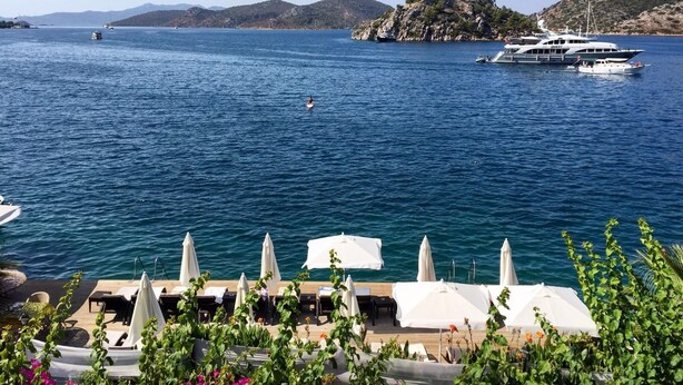 A waterfront property with a pool area, lounge chairs, and umbrellas. - Yılmaz Kaptan Otel (Marmaris)