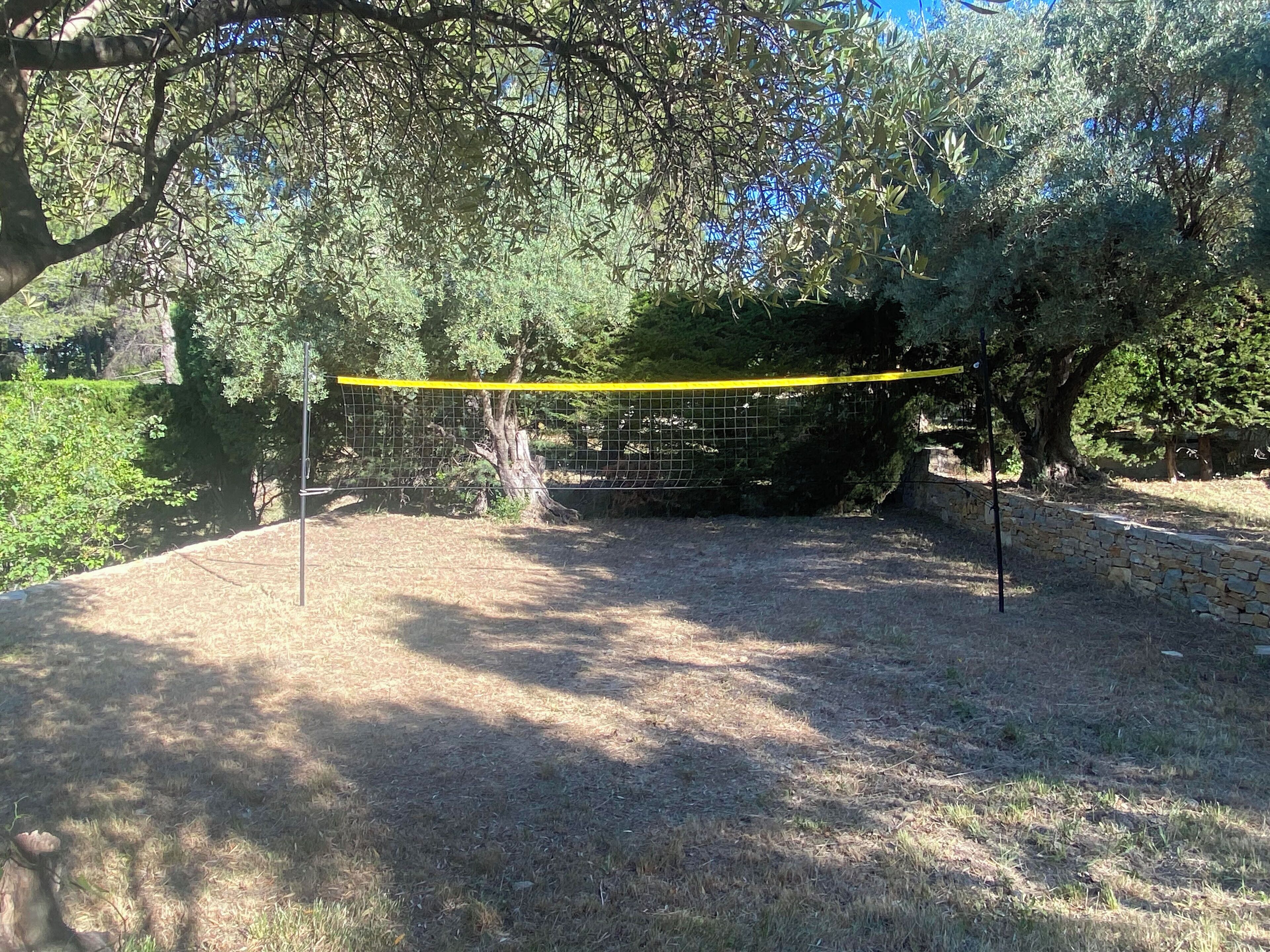 An outdoor area with a yellow netted enclosure, surrounded by trees and a stone wall.