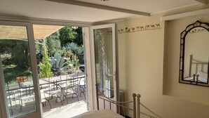 Une chambre avec un lit, un miroir et une vue sur une terrasse extérieure aménagée avec des chaises et des plantes.