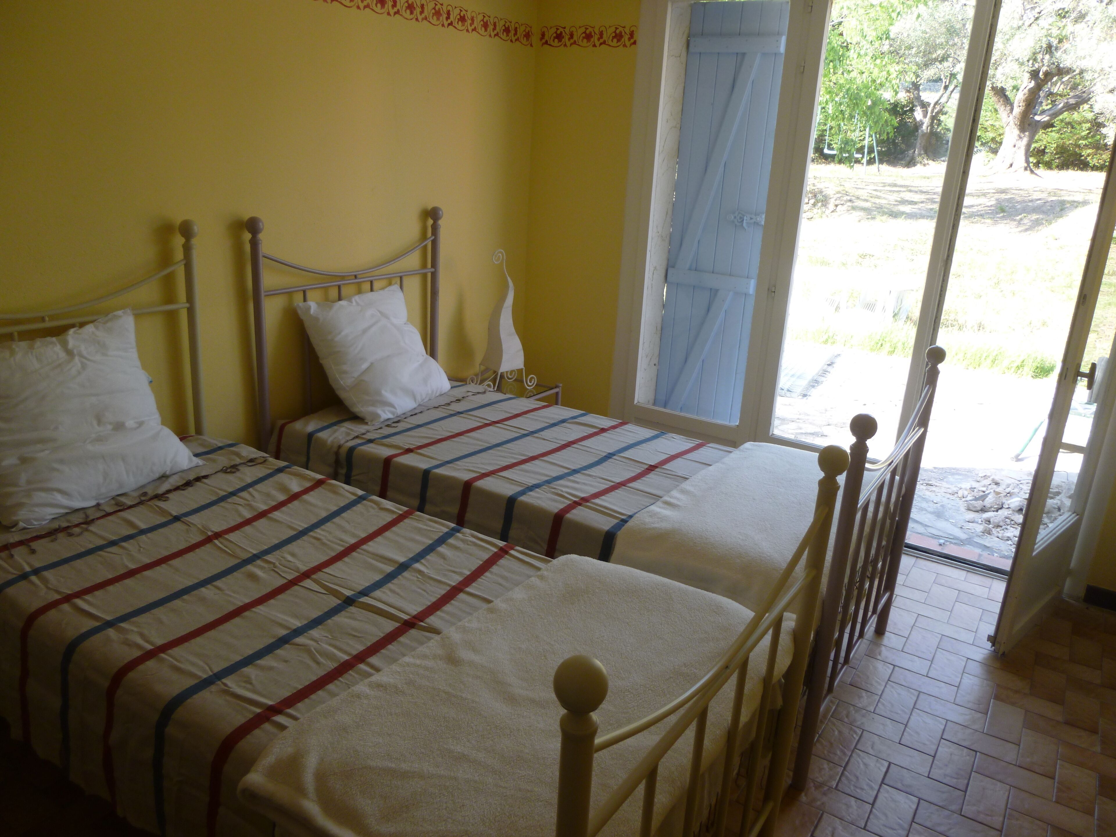 Habitación con dos camas, cada una con una colcha a rayas y almohadas blancas. Se ve una ventana con vistas al exterior.