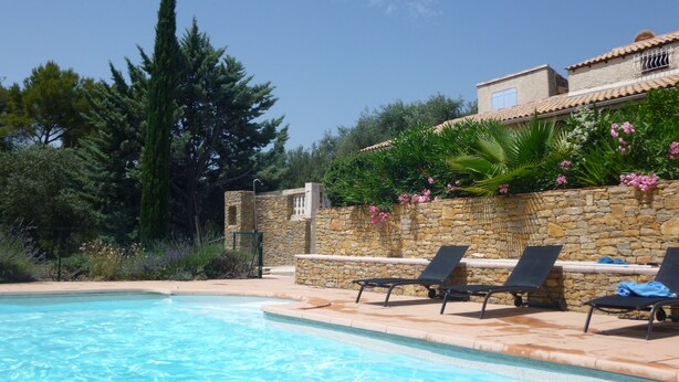 Un espace piscine avec des chaises longues, un mur en pierre et un bâtiment doté d’un toit en tuiles.