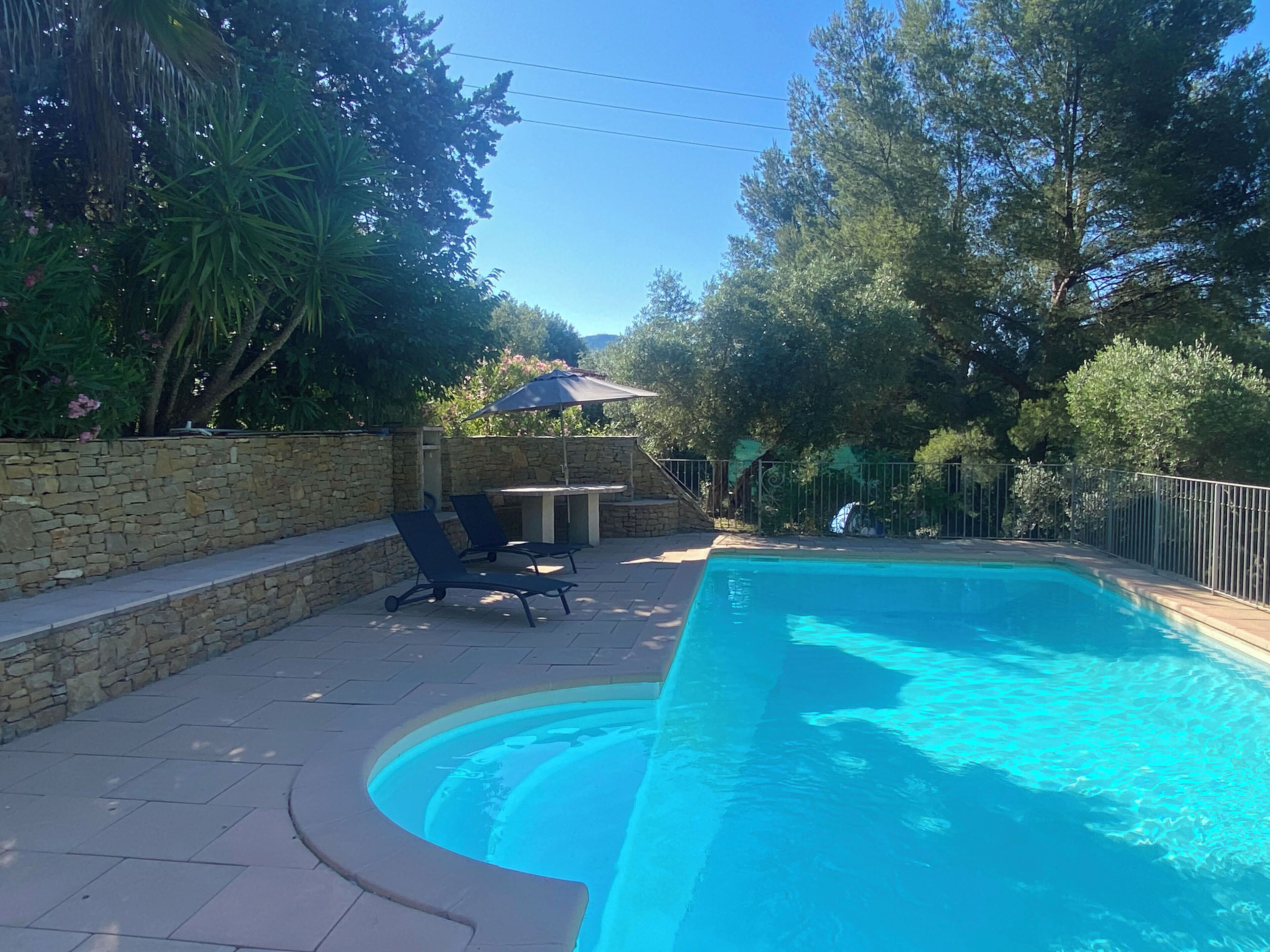 A swimming pool with a stone wall and lounge chairs.