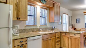 A kitchen with wooden cabinets, a granite countertop, a built-in dishwasher, and a window with blinds.