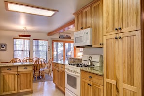 Una cocina con armarios de madera, estufa a gas, microondas y un comedor con sillas y mesa.