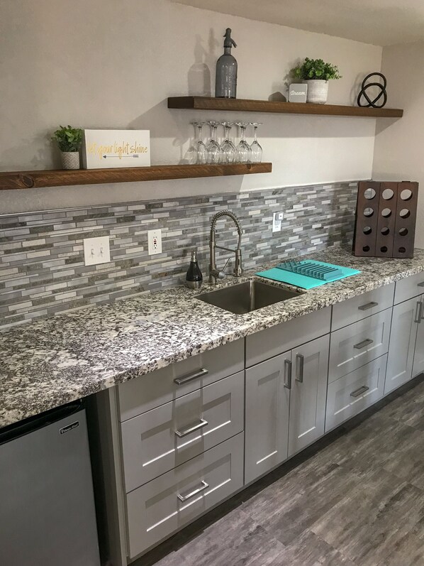 Una cucina con un piano di lavoro in granito, elettrodomestici in acciaio inossidabile e una parete di fondo rivestita con piastrelle grigie.